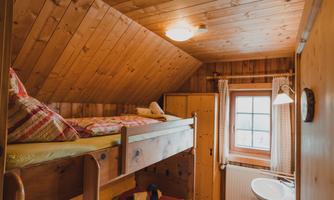 A cozy room with wooden paneling and a bunk bed. The window lets in plenty of daylight and offers a view of nature.