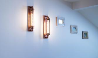 Two stylish wall lights shine on a white wall. Next to them, various small picture frames are hanging.