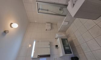 A modern bathroom with white tiles. It features a bathtub, a shower, and a large mirror.