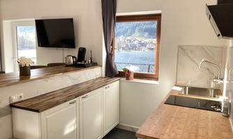 A modern kitchen with a wooden countertop and white cabinets. A window offers a beautiful view of the mountains and a lake.