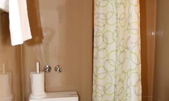 A small bathroom with a shower and a toilet. The walls are painted in a warm brown tone, and the shower curtain has a green pattern.