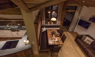 A cozy living kitchen with wooden furniture and a large dining table. Lots of light streams through the windows, creating an inviting atmosphere.