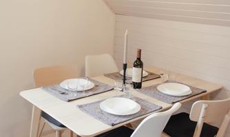 A cozy dining area with a table and four chairs. On the table are plates, a bottle of wine, and a candle.