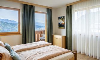 A modern bedroom with two beds and large windows. The view shows mountains and a tranquil atmosphere.