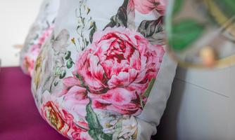 A beautiful cushion with colorful floral patterns on a violet background. In the background, soft colors and a cozy atmosphere can be seen.