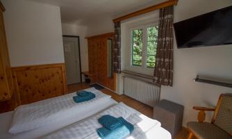 A cozy room with two beds and blue towels. There is a window that offers light and a view outside.