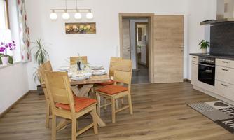 A bright dining room with a round table and four chairs. In the background, a modern kitchen is visible.