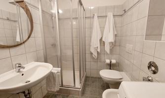 A modern bathroom with a shower, a sink, and a toilet. The walls are tiled with white tiles and are clean and bright.
