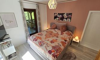A cozy bedroom with a large bed and colorful pillows. The walls are painted in soft colors and there are natural light sources.
