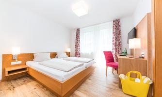 A modern bedroom with two single beds and a wooden floor. Next to the bed is a table with a television and a chair.