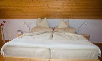 A cozy bedroom with a large bed and bright pillows. The walls are made of wood, creating a warm atmosphere.