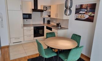 A modern kitchen with bright cabinets and a round table. Green upholstered chairs complement the elegant design.
