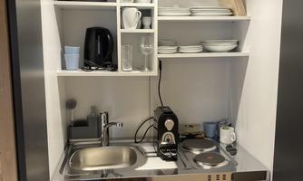 A modern kitchen unit with stainless steel surface and various appliances. Dishes and kitchen utensils are neatly organized above.