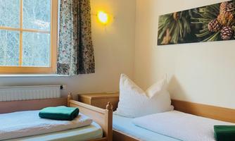 A simple room with two single beds and a green carpet. The windows let in plenty of daylight and the walls are painted in bright colors.