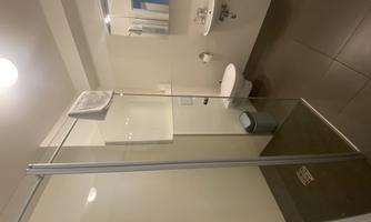 A modern bathroom with a shower and a sink. The walls are light and the floor is dark, featuring a clean and minimalist decor.