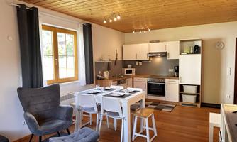 A modern kitchen with a dining area and cozy chairs.  
Bright walls and a wooden ceiling create an inviting atmosphere.