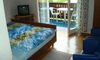 A cozy bedroom with a large bed and blue pillows. There is a small balcony with a table and chairs, as well as a television in the room.