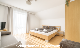 A bright bedroom with a large double bed and a window that lets in plenty of daylight. There is a television and modern furniture that creates a cozy atmosphere.