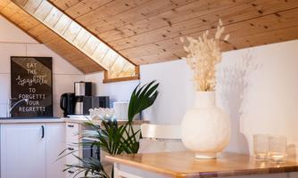 A cozy kitchen with wooden walls and a wooden counter. A decorative vase with dried flowers and a large plant branch is on the table.