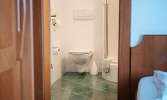 A bathroom with a shower, toilet, and modern tiles. The entrance to the bathroom is visible through a wooden door.