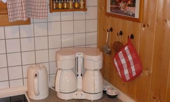 A cozy kitchen with a coffee machine and a kettle on a granite countertop. Spices and a red dish towel hang on the wall.