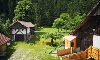 A peaceful courtyard with two traditional buildings and a playground. Surrounded by trees and green grass, the landscape offers a relaxing atmosphere.