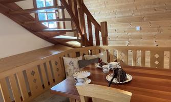 A cozy dining area with a wooden table and benches. A staircase leads to the upper floor, surrounded by warm wood paneling.