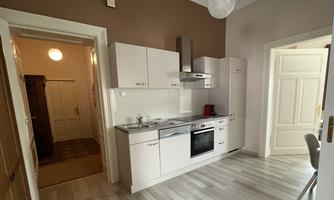 A modern kitchen with white cabinets and a light wood floor. The room is well-lit and has an inviting atmosphere.