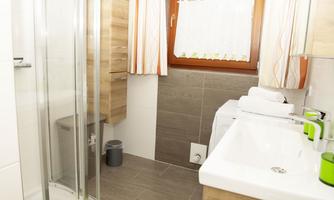 A modern bathroom with a shower, sink, and wooden shelf. Bright curtains let light in and create a friendly atmosphere.