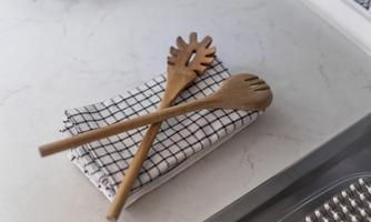 Two wooden cooking spoons lie on a striped kitchen towel. The background features a bright and modern kitchen countertop.