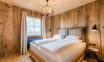 A cozy bedroom with wooden walls and a large bed. The room has a window with a view outside and stylish lighting.