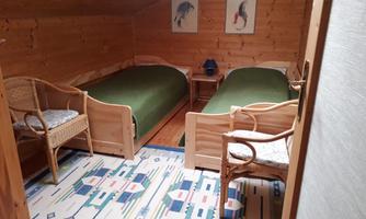 A cozy room with two single beds and wood-paneled walls. There is a small table and two chairs, as well as decorative pictures on the wall.