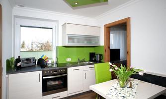 A modern kitchen with green accents and wooden details. The table is decorated with a flower vase and offers an inviting atmosphere.