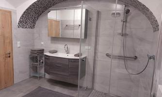 A modern bathroom with a spacious shower and an elegant sink. The walls are in light gray tones, and there is a practical towel rack.