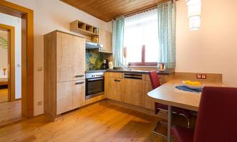 A modern kitchen with wooden shelves and a stove. The room feels bright and inviting, with a dining table and chairs in a red design.