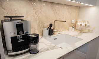 A modern kitchen corner with an elegant espresso machine and a sink. The marble countertop creates a stylish atmosphere.