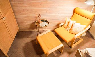 A cozy room with an orange armchair and a matching table. A wooden box stands against the wall, and a small book lies on the table.