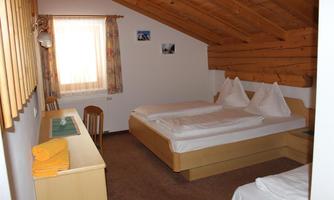 A cozy bedroom with two beds and a clear wood decor. The room has a window with curtains and simple furniture.