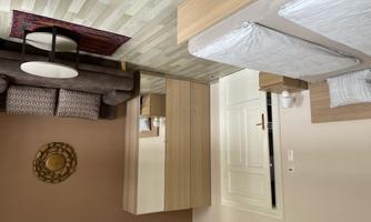 A cozy bedroom with a double bed and brown wall paint. There is a wardrobe and a sitting area with a sofa and a table.