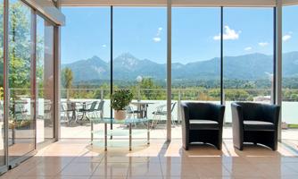 A bright room with large windows and a view of the mountains. Two black armchairs are arranged around a glass table.