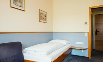 The Small Single Room at Hotel Hecher in Wolfsberg is the ideal choice for solo travelers who value comfort in a compact space. The room offers a comfortable single bed, a small sofa, and practical storage areas. Warm wooden elements, soft blue tones, and friendly lighting create a calm, pleasant atmosphere – perfect for business travelers or short stays.