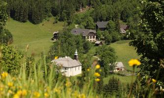 A picturesque landscape with gentle hills and a small village. Between the green meadows, some residential houses and a church can be seen.