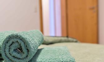 A stack of green towels is neatly placed on a bed. In the background, a closed door is visible.
