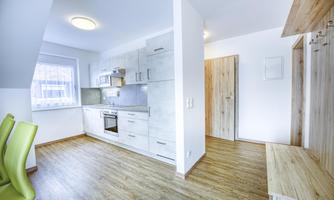A modern kitchen with bright cabinets and an open living area. The floor is made of wood and the walls are painted light.