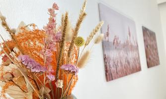 A beautiful bouquet of pink and orange dried flowers is in a vase. In the background, delicate pictures can be seen on the wall.