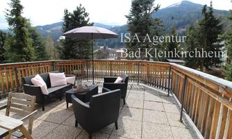 A cozy balcony with black garden furniture and a sunshade. In the background, mountains and trees can be seen.