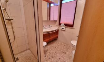 A modern bathroom with a shower, sink, and toilet. The walls are brightly tiled, and there is a window with a roller shutter.