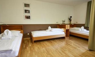 A simple, bright room with three single beds. The floor is made of wood and there are decorative pictures on the wall.