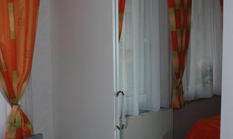 A bright room with orange curtains and a bed in the background. The window lets in a lot of daylight.