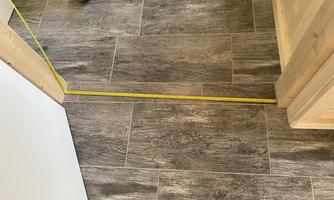 A beautifully laid floor with tiles in wood look. A measuring tape measures the distance between two walls.